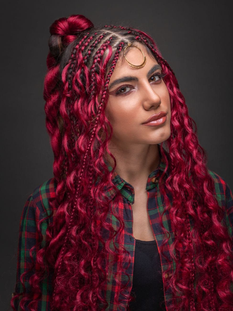 Trendy young ethnic woman with wavy threads in braids and ring on forehead looking at camera on gray background