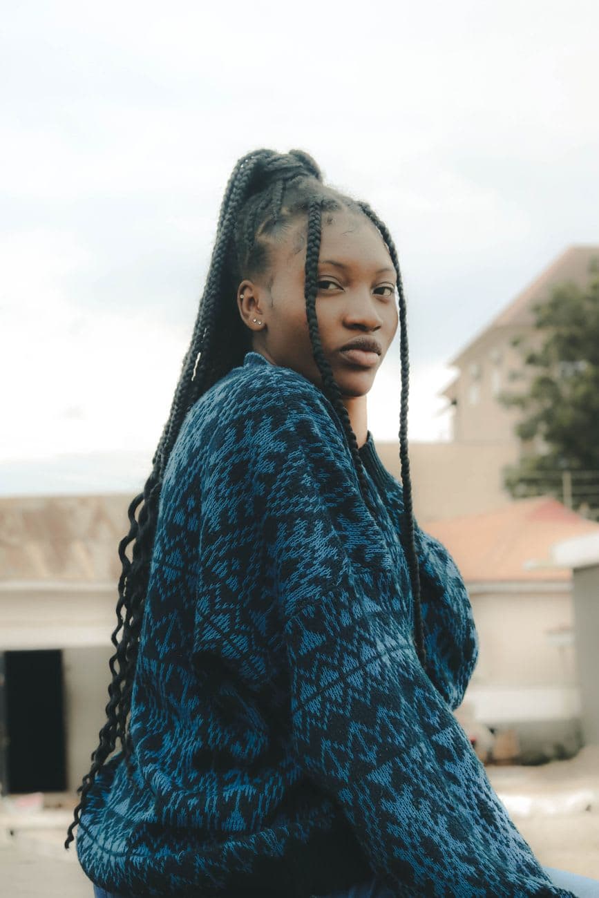 Portrait of a young woman with braided hair, wearing a blue sweater, sitting outside.