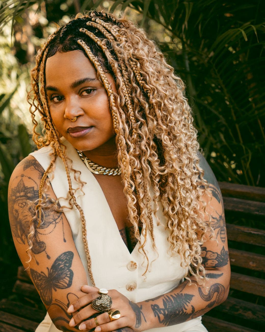Portrait of a confident woman with tattoos and braided hair sitting on a bench outdoors.
