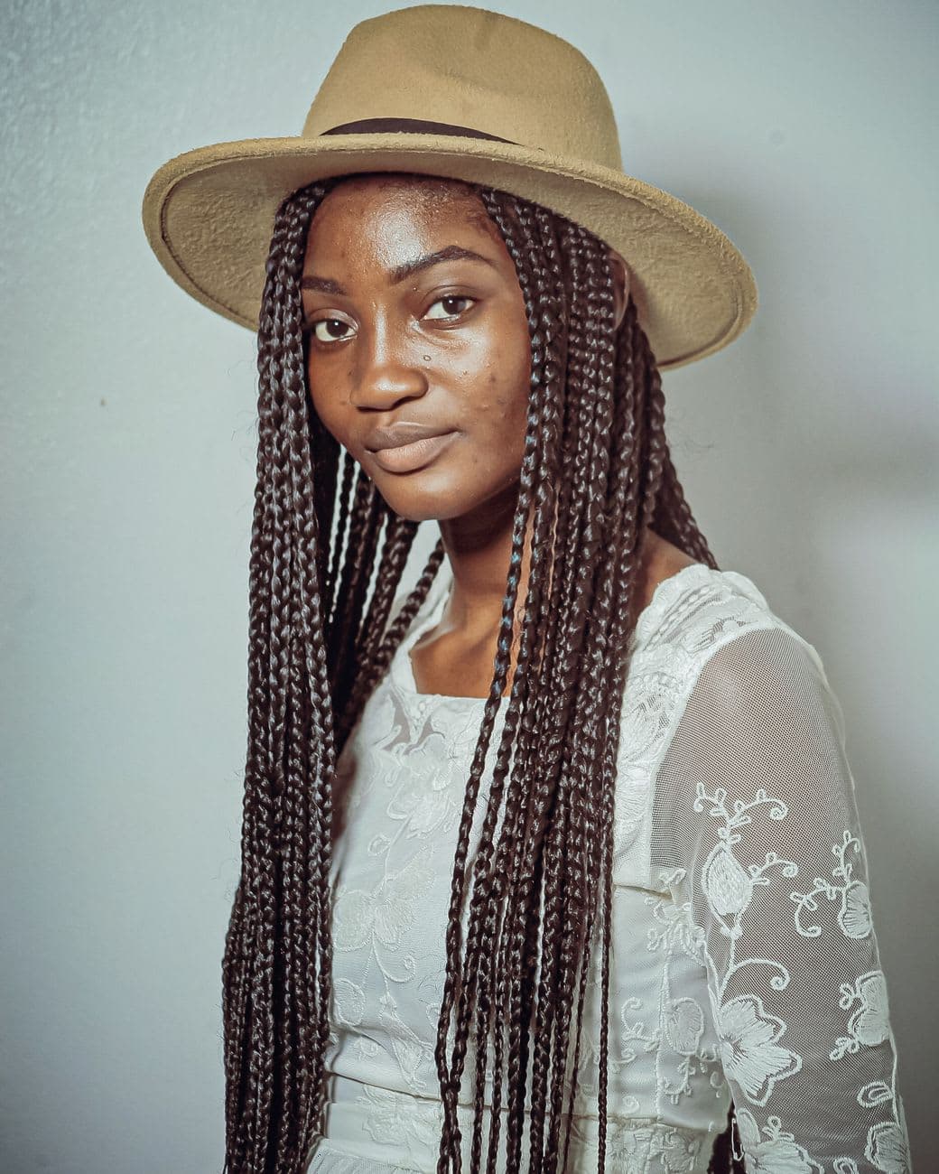 Elegant portrait of a woman in braids wearing a stylish hat and lace dress.
