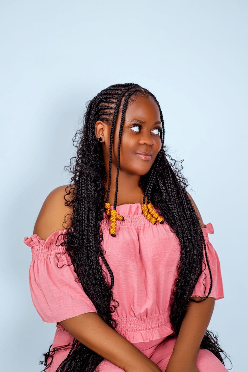 Portrait of a smiling young woman in a pink outfit, featuring long braided hair with beads.