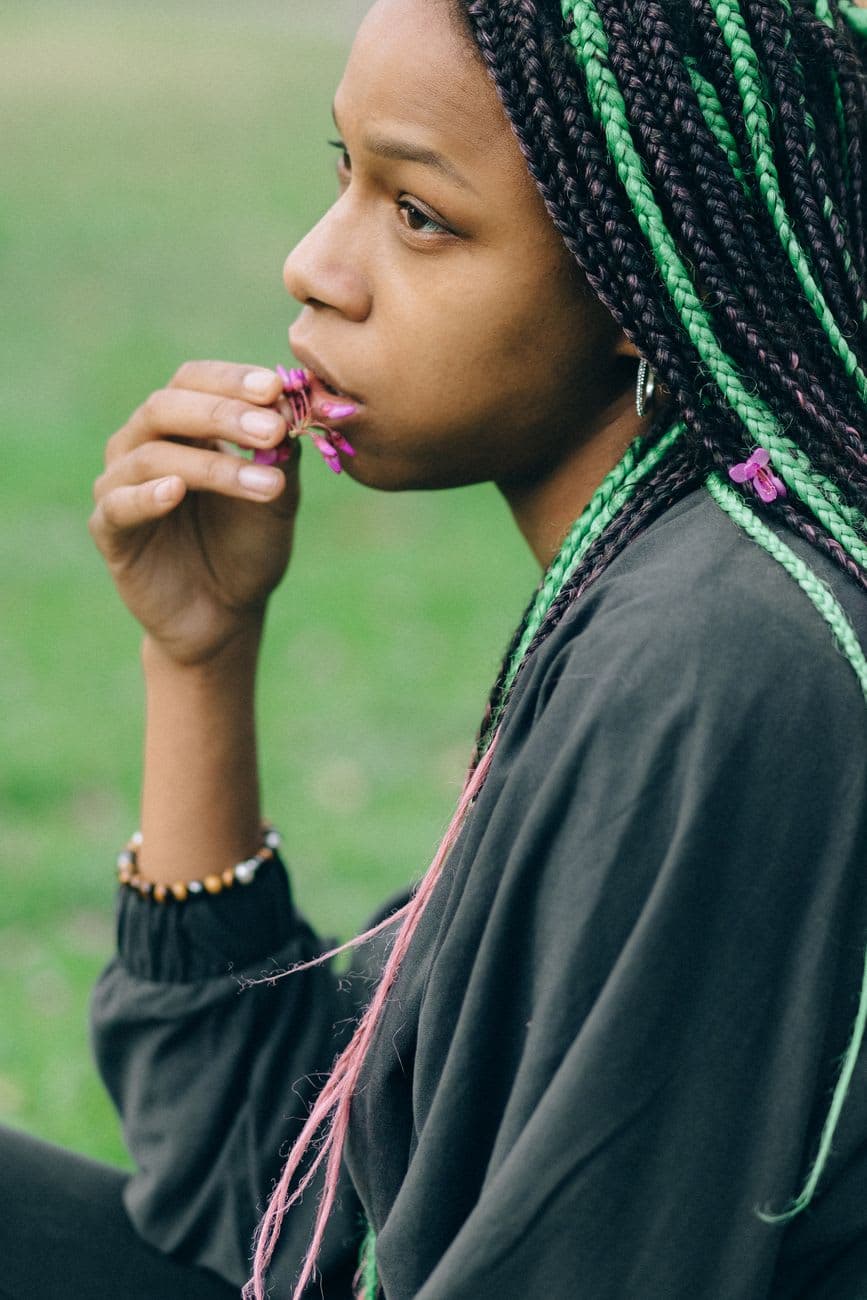 Portrait of a black woman with braided hair holding a flower, seated outdoors.
