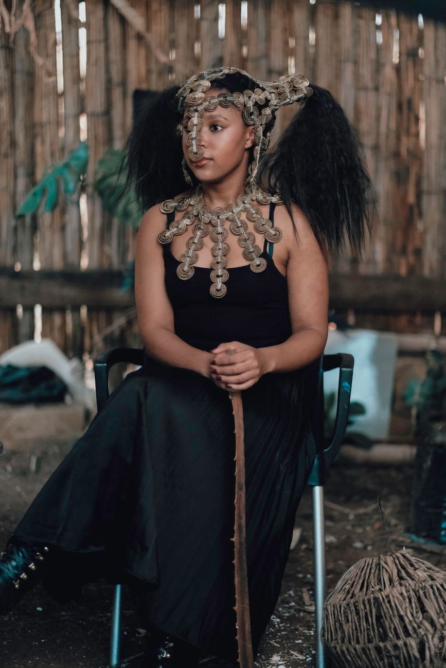 Woman seated indoors, wearing ornate African jewelry and black dress.