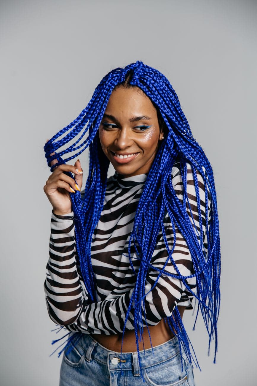Stylish woman with bright blue braided hair posing confidently indoors.