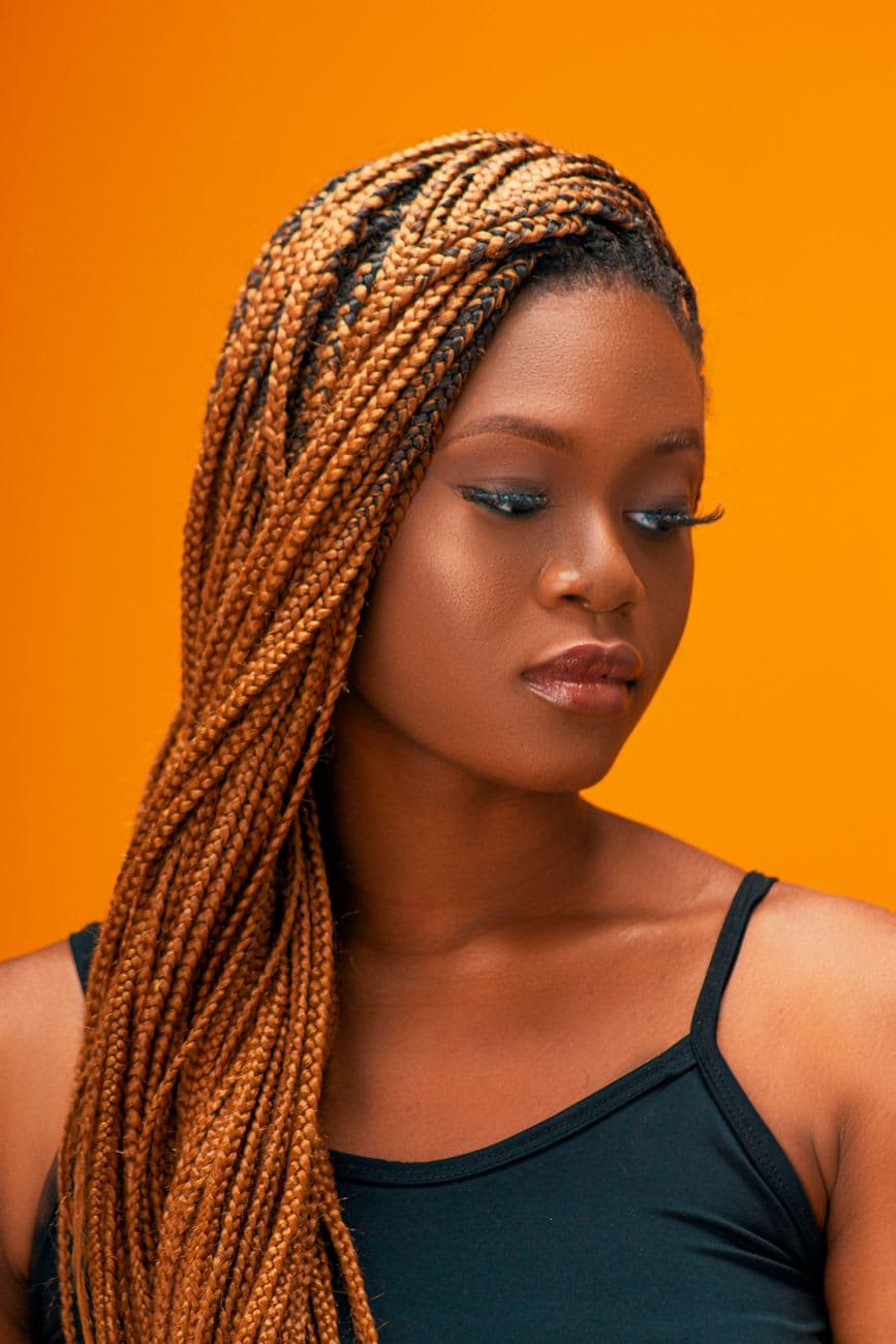 Stunning portrait of a black woman with box braids against a vivid orange backdrop.