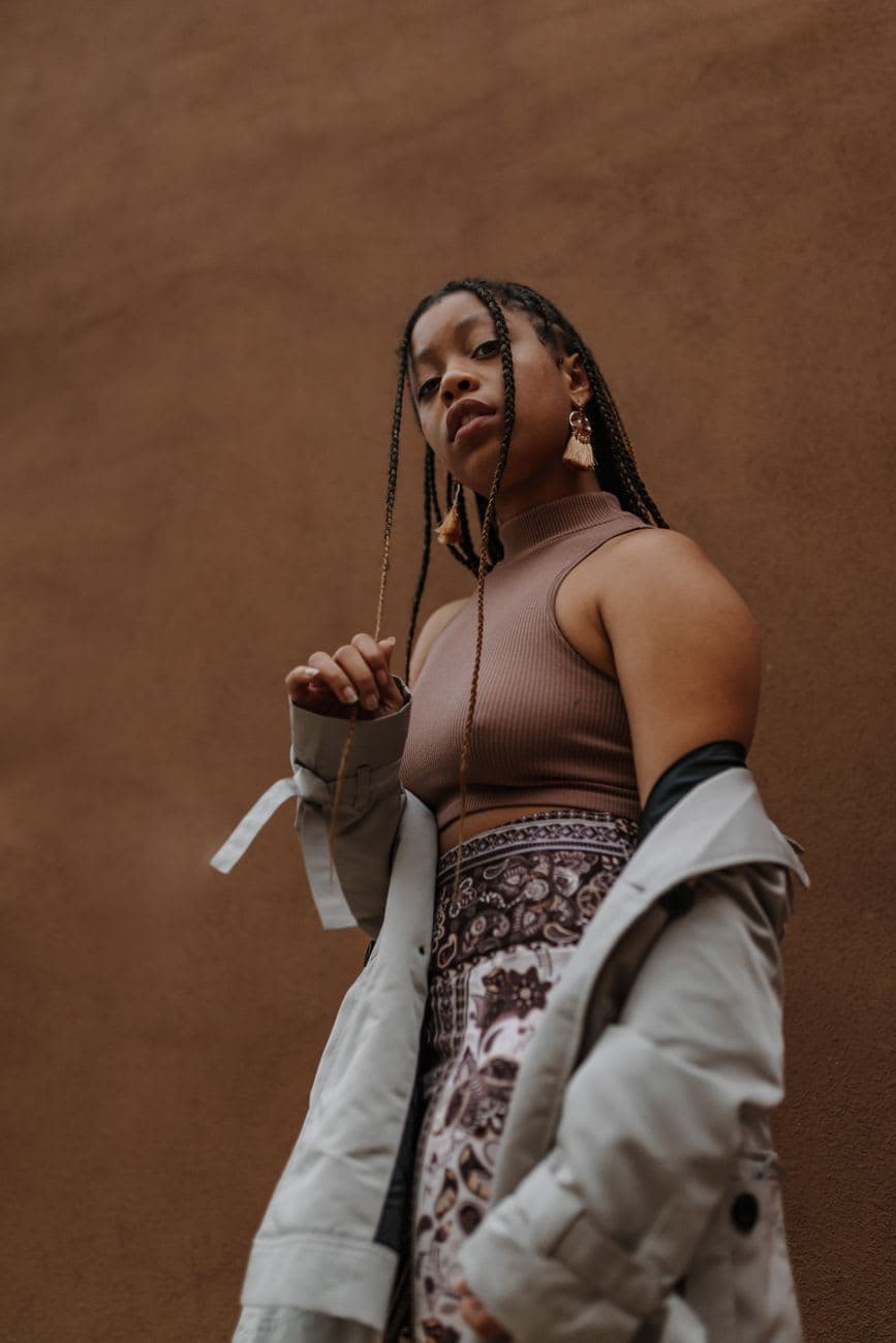 Portrait of a woman with box braids and chic outfit against a brown background, exuding confidence.