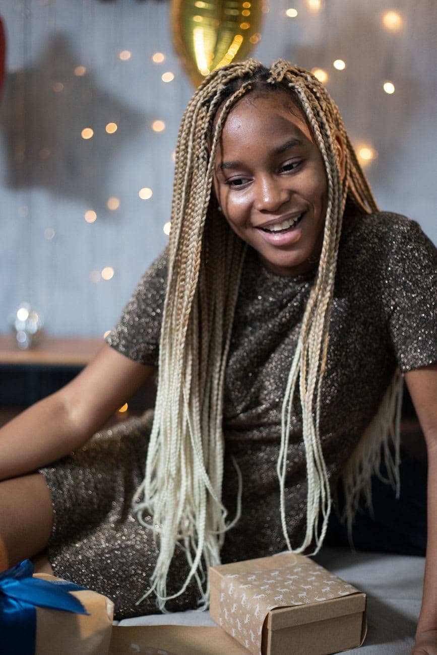 African American woman with gifts enjoys indoor celebration, surrounded by warm lights.