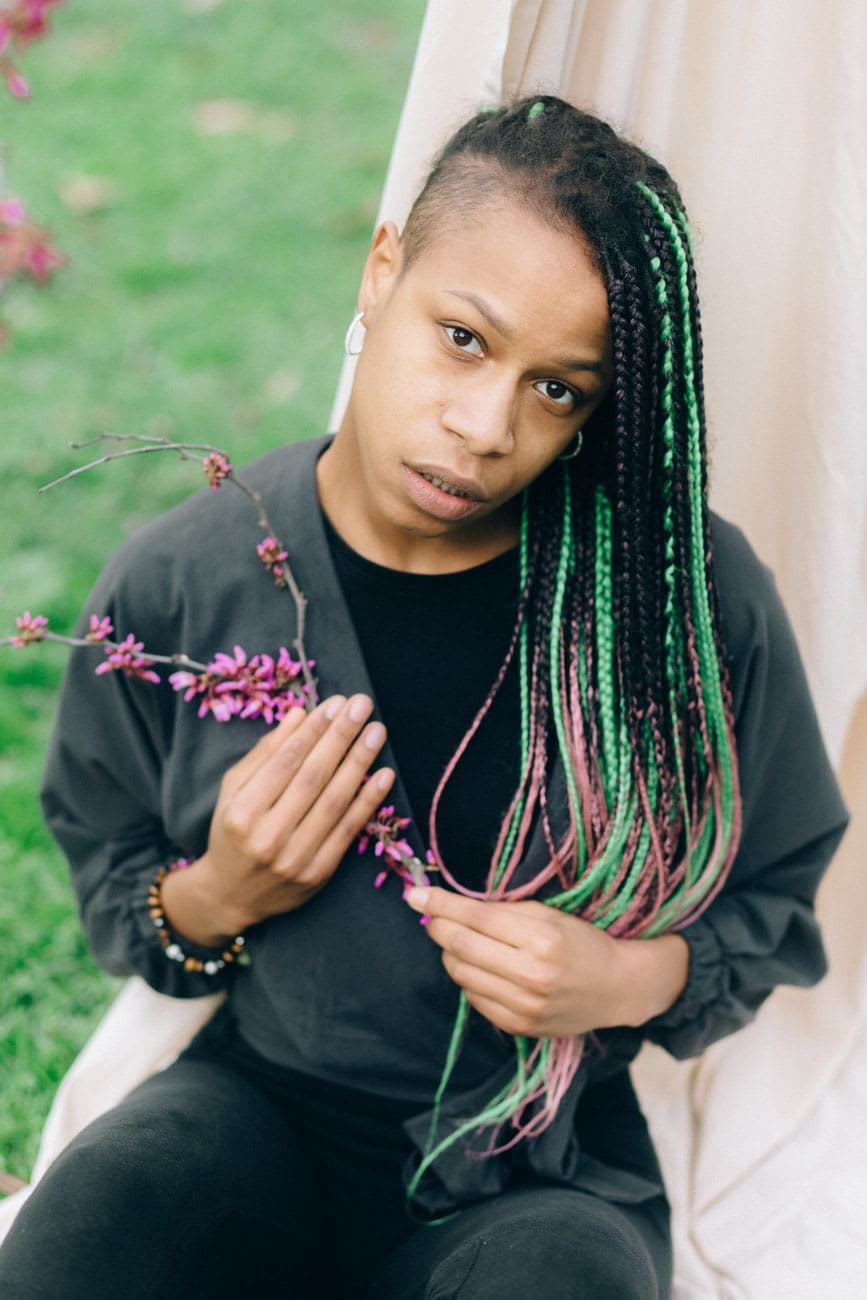 A woman with braided hair holds flowers in a serene outdoor setting.