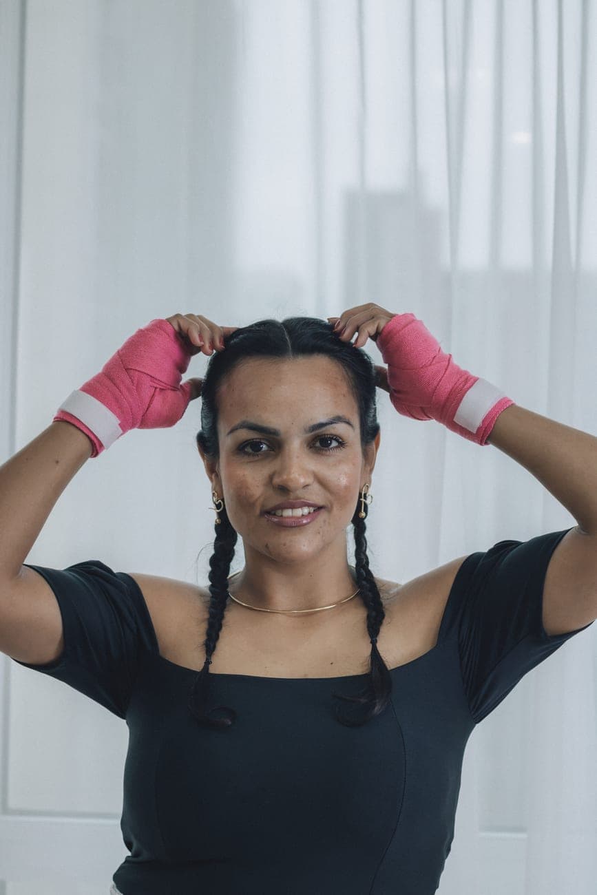 Portrait of a woman indoors, wearing pink boxing wraps and braided hair, exuding confidence.