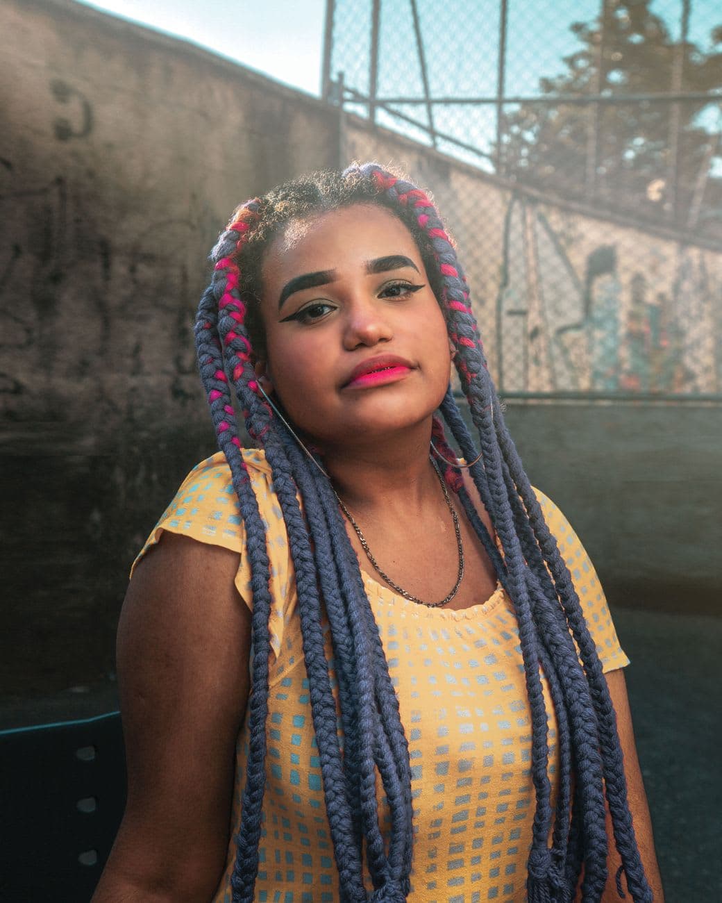 Portrait of a young woman with vibrant braids standing outdoors, exuding confidence and style.