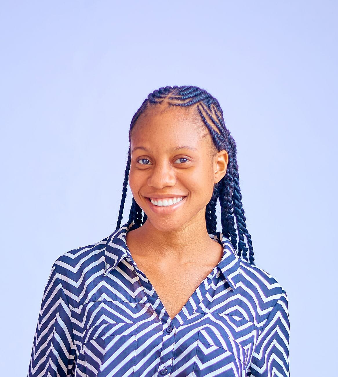 Portrait of a smiling woman with braided hair wearing a patterned shirt against a light background.