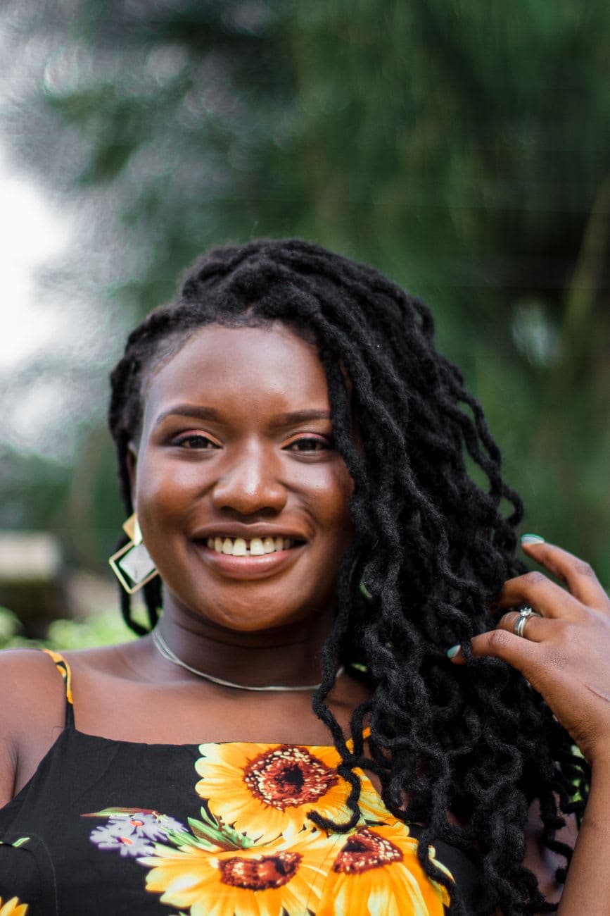 Close-up of a smiling woman with locs wearing a floral dress, outdoors in Nairobi.