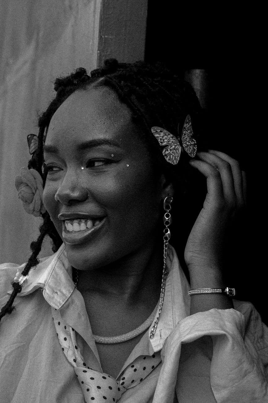 Black and white portrait of a smiling woman with butterfly accessories enhancing her hairstyle.