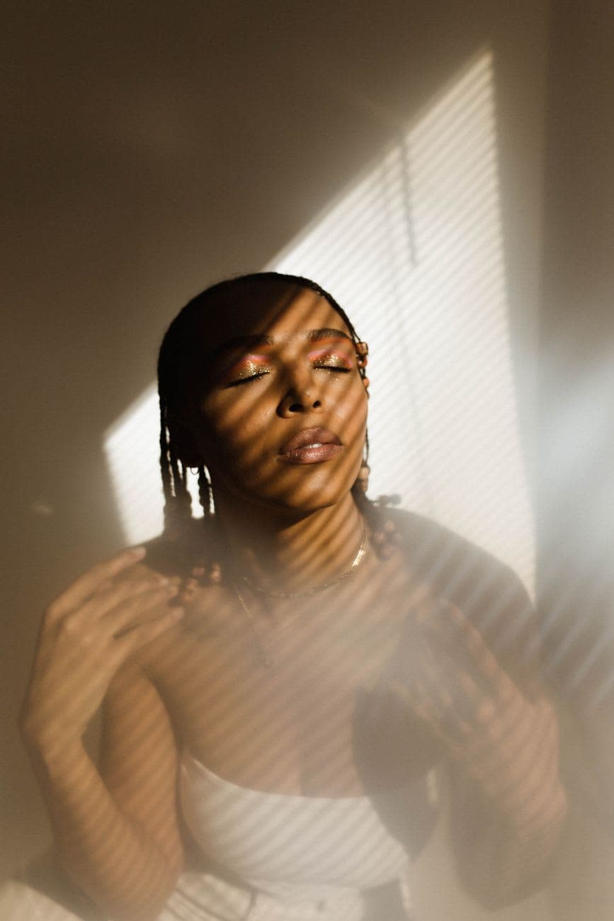 Portrait of a woman with cornrows in artistic shadows, eyes closed, in a studio setting.