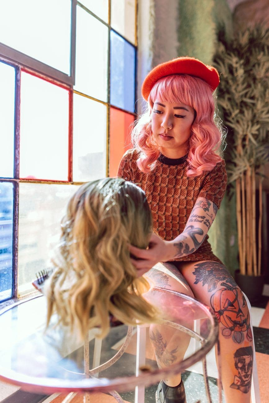 A young woman styles a wig in a colorful indoor setting, showcasing modern hair fashion.