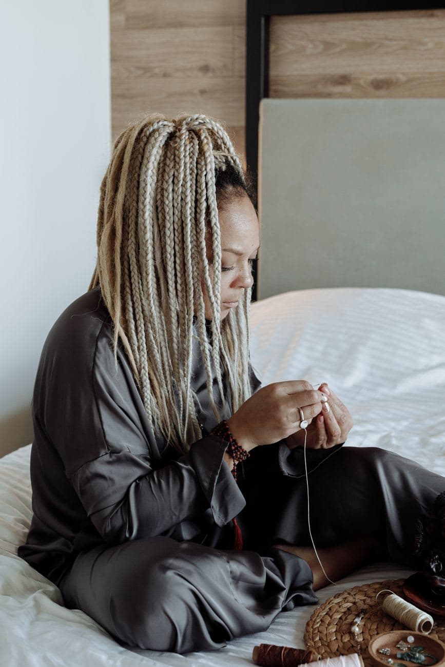 A woman with braids focused on sewing in a cozy bedroom setting.