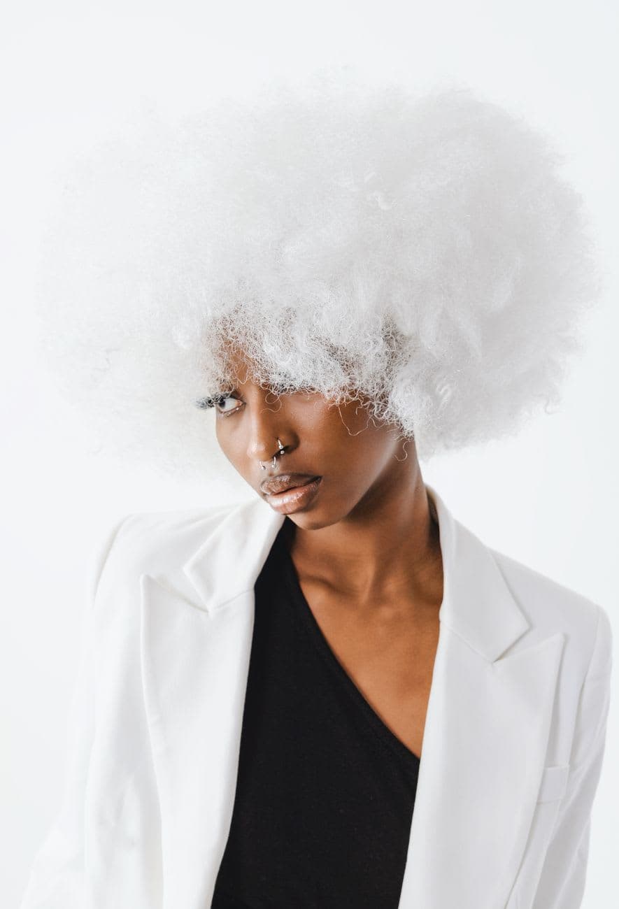 Elegant studio portrait of a fashionable woman with a fluffy white afro wig and chic attire.