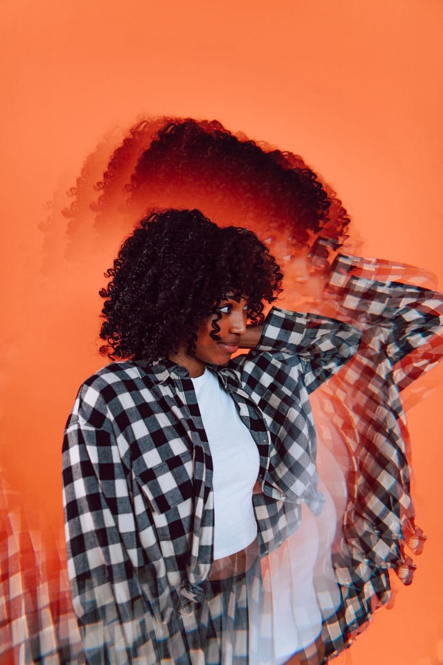 Creative portrait of a woman with curly hair wearing plaid, captured against vibrant orange.