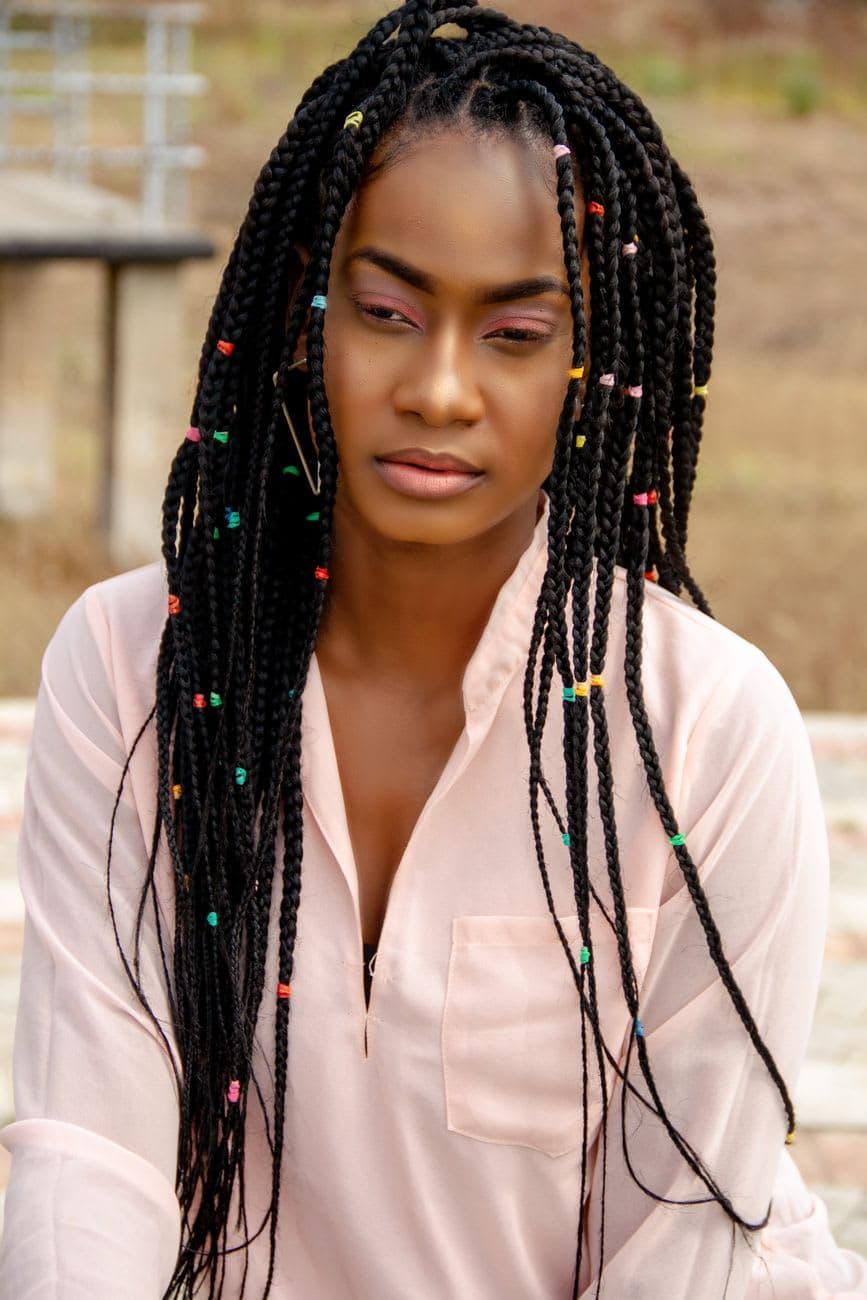 A chic portrait of a woman with colorful braided hairstyle wearing white long sleeves outdoors.