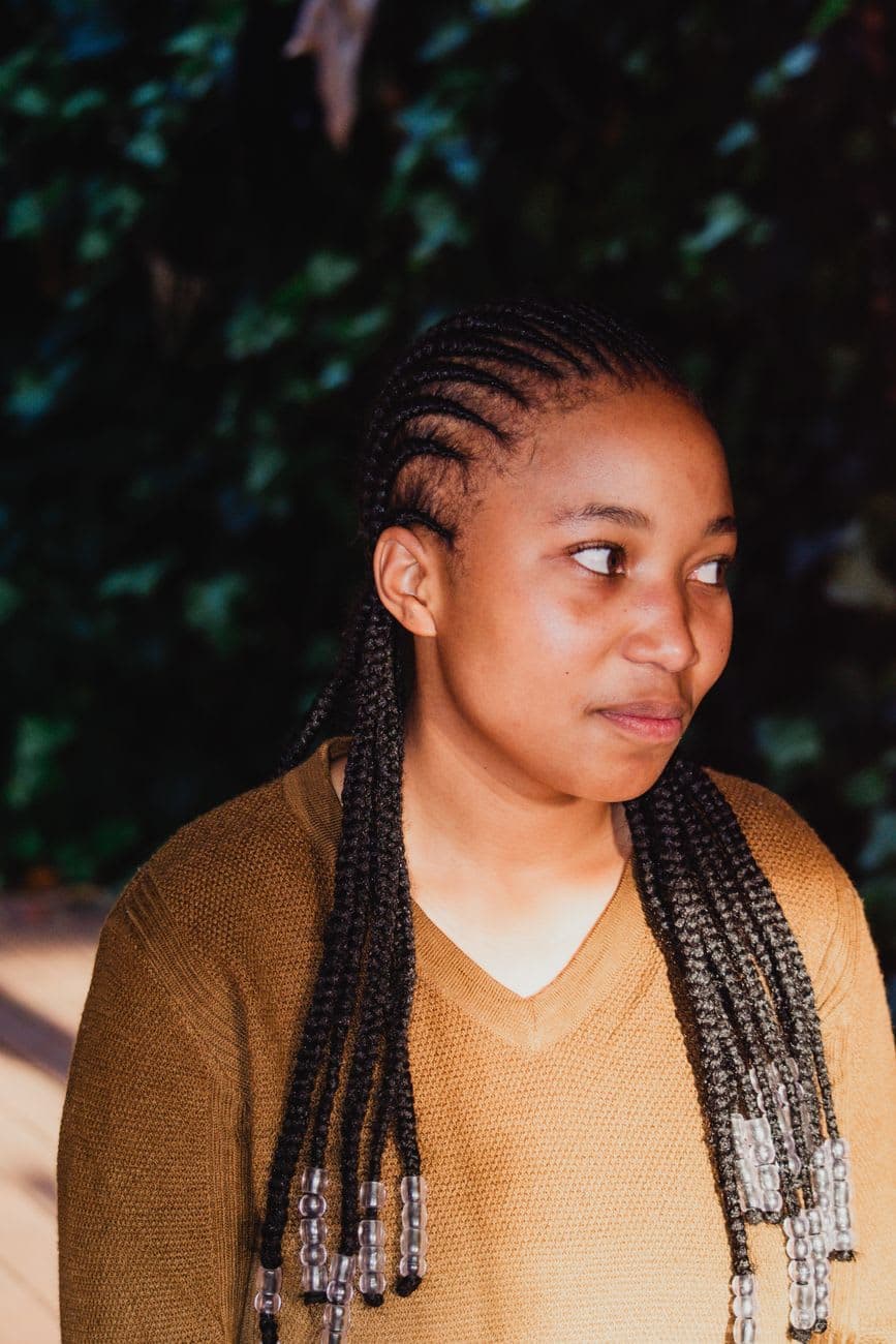 Charming portrait of a young girl with braided hair wearing a brown shirt outdoors.