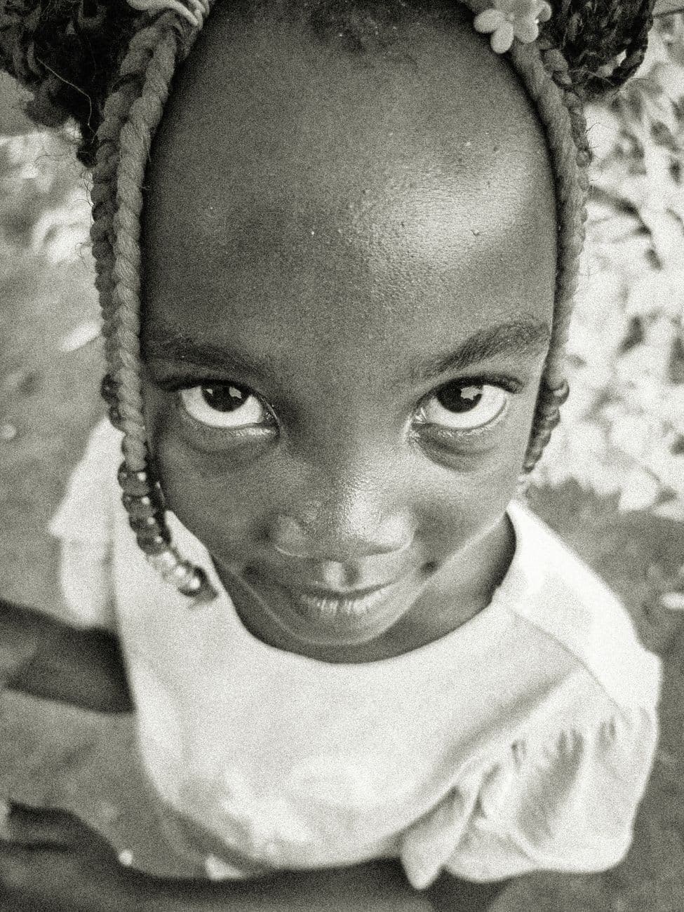 Black and white portrait of a child with braided hair looking at the camera.