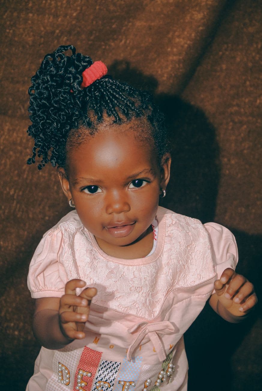 Charming portrait of a young Nigerian girl in a pink dress with braided hair.