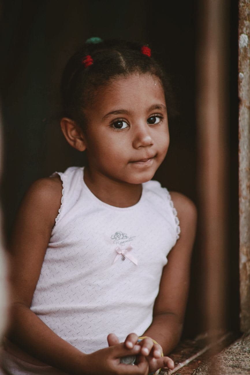 A delightful portrait of a young girl with braided hair in a white tank top, captured indoors.