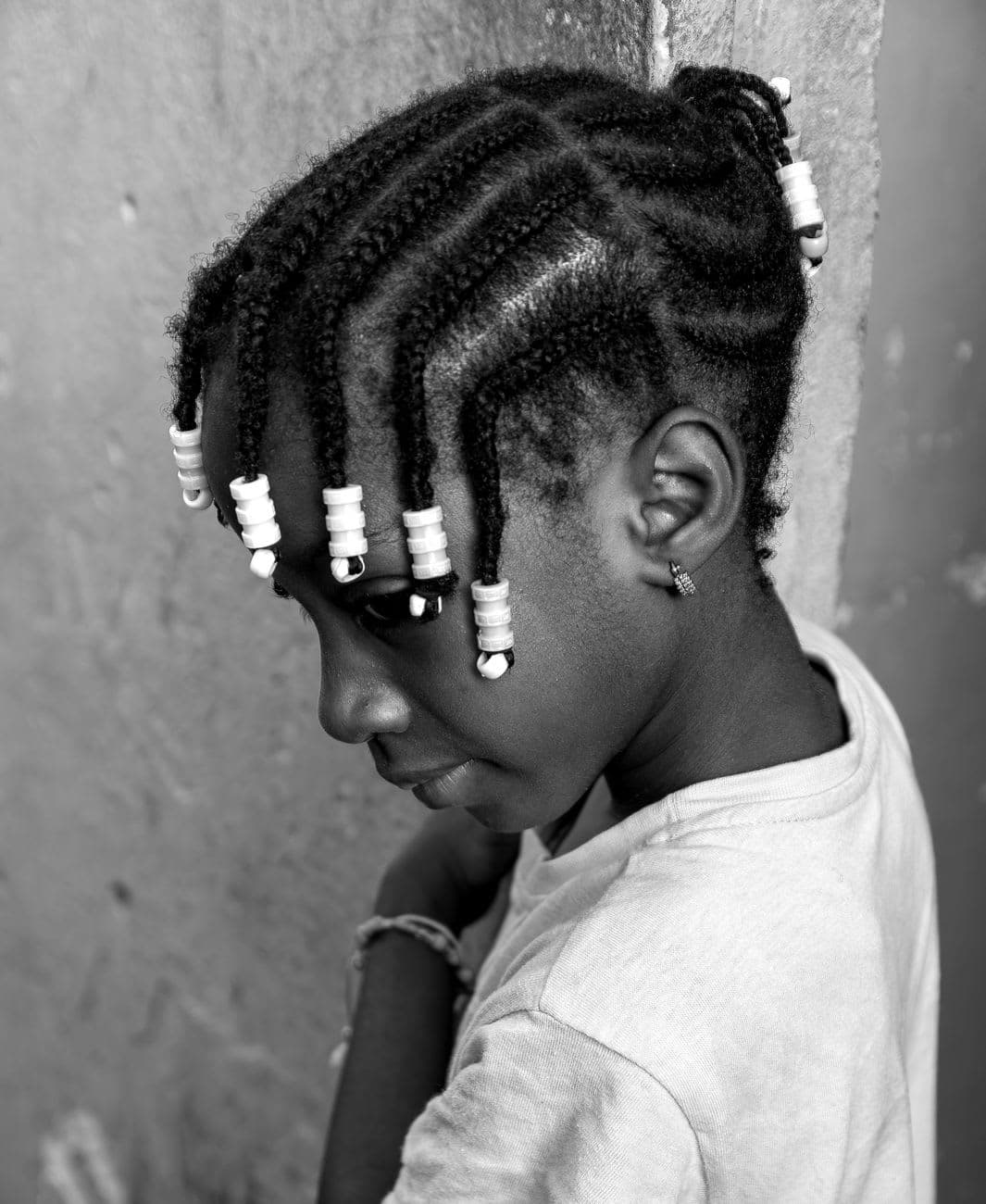 Black and white portrait of a girl with braided hair and beads, expressing contemplation.