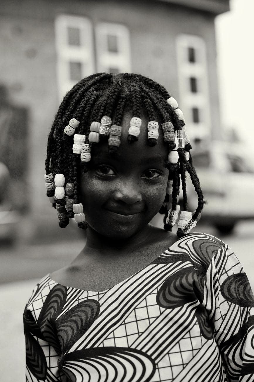 Smiling Nigerian girl in traditional attire with braided hair outdoors.