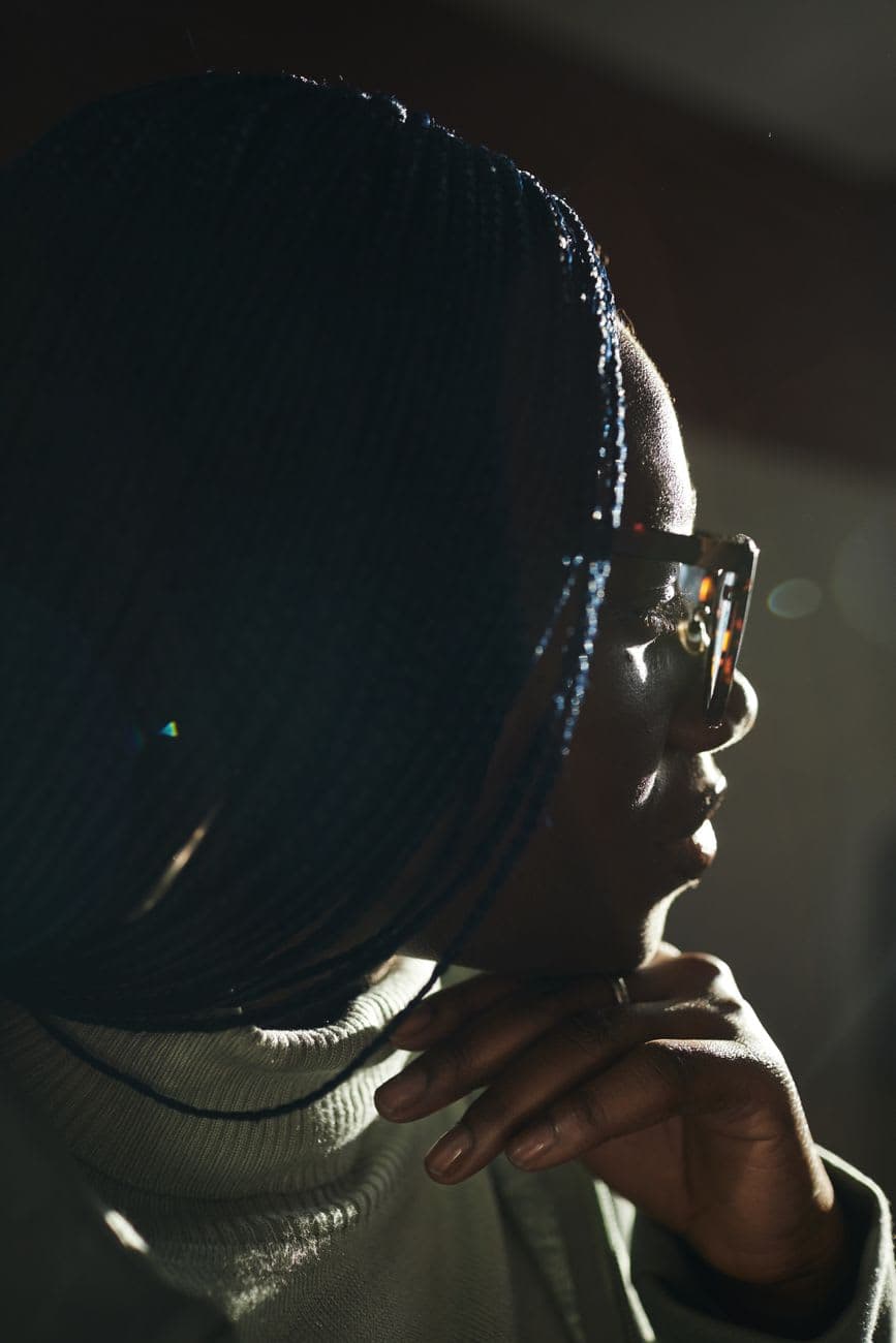 Side profile of a woman with braided hair and eyeglasses, captured in soft lighting.