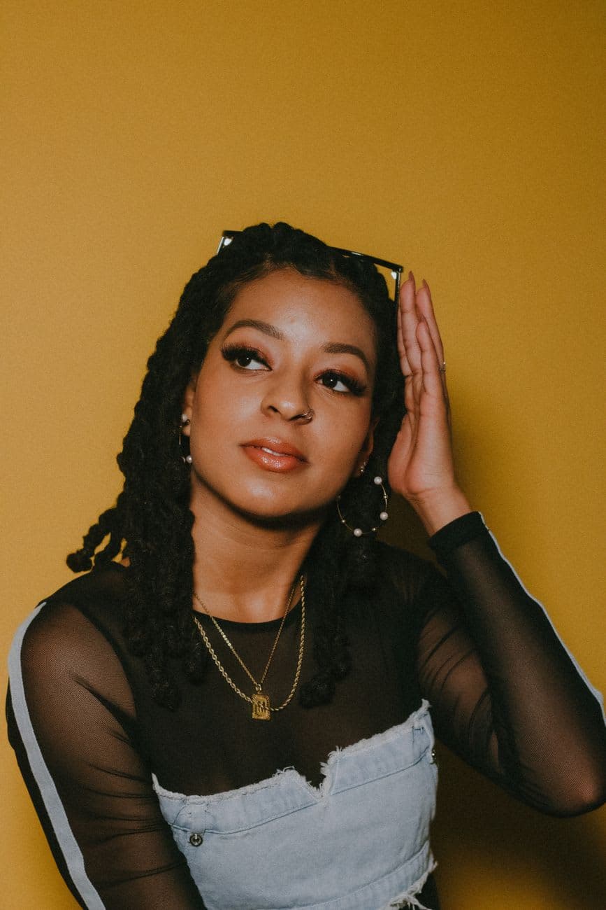 Fashion portrait of a stylish woman with twists and a bold look against a yellow backdrop.