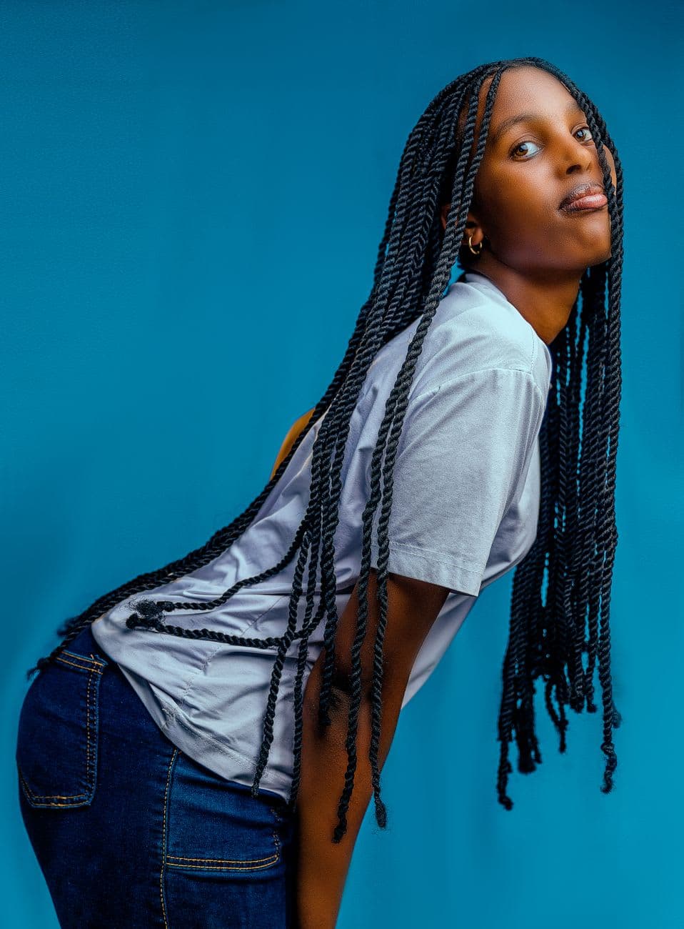 Woman in casual outfit posing with long braided hair against a blue background.
