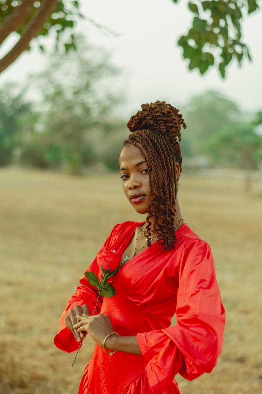 Portrait of an African woman in a vibrant red dress holding a rose in an outdoor setting.