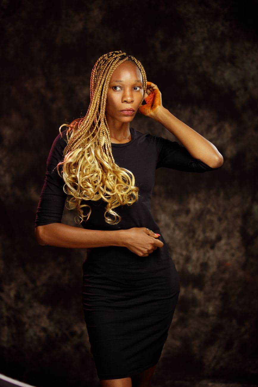Elegant portrait of an African American woman in a studio setting wearing a black dress and braided hairstyle.