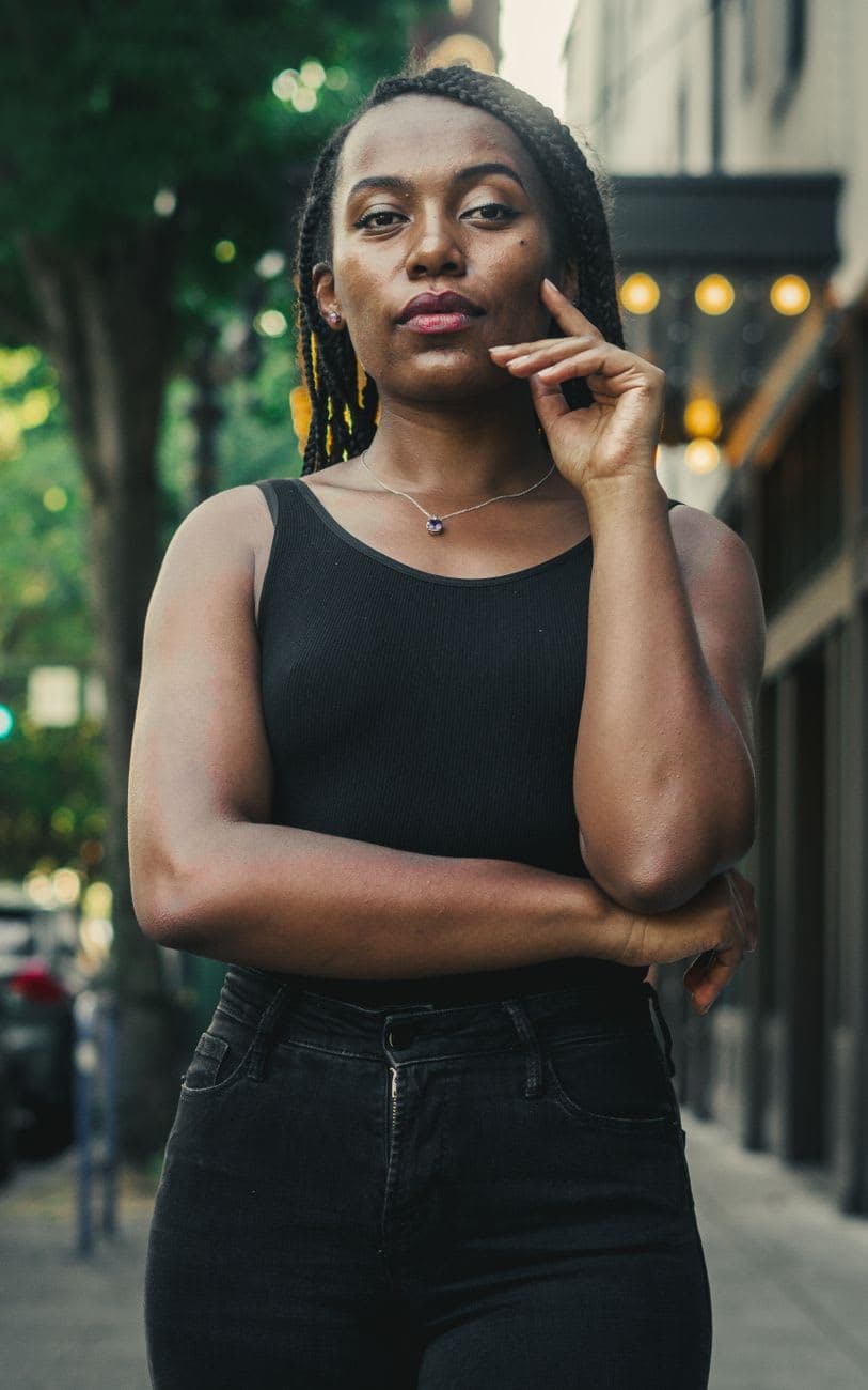 Fashionable black woman with braids posing confidently in an urban outdoor setting.