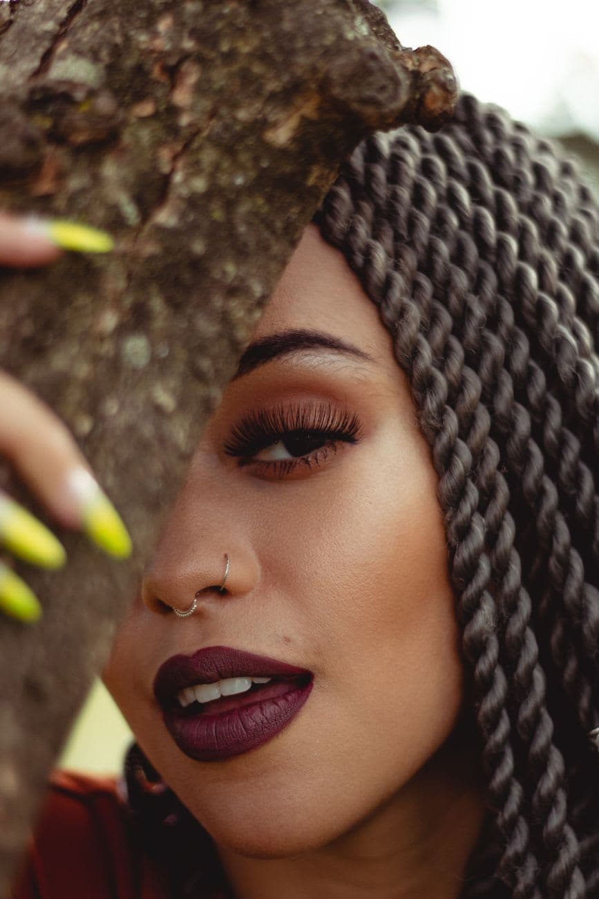Close-up portrait of a woman with twisted hair, bold makeup, and nose ring.