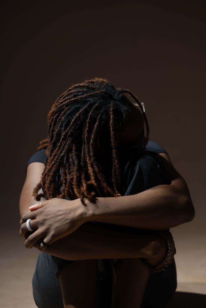 Artistic portrait of a woman hugging knees, dreadlocks styled, dramatic lighting.