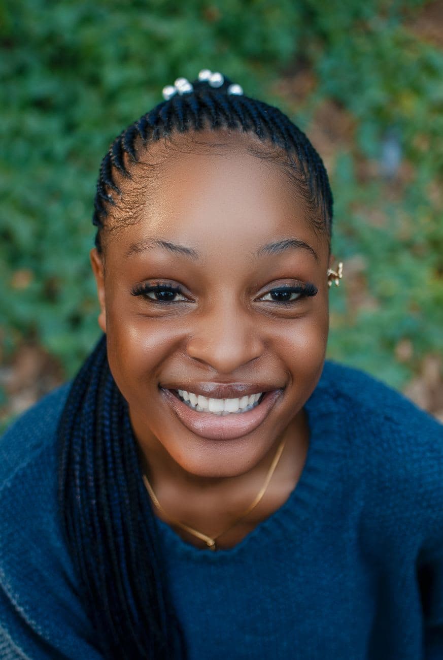 Cheerful young woman with braided hair smiling brightly outdoors in Ibadan, Nigeria.