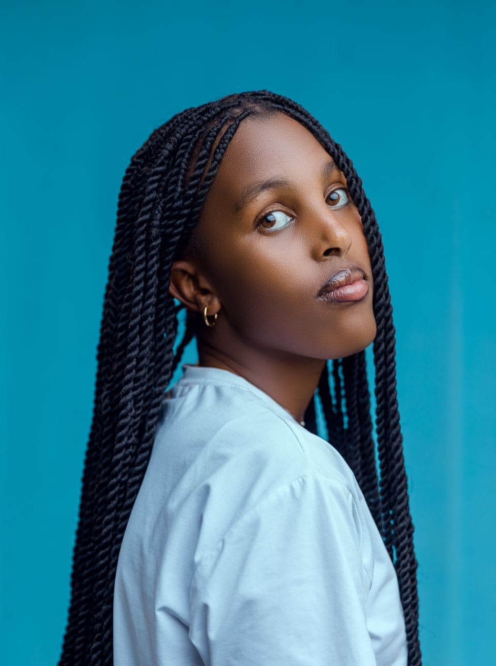 Woman with long braided hair posing against a bright blue background, exuding style and confidence.